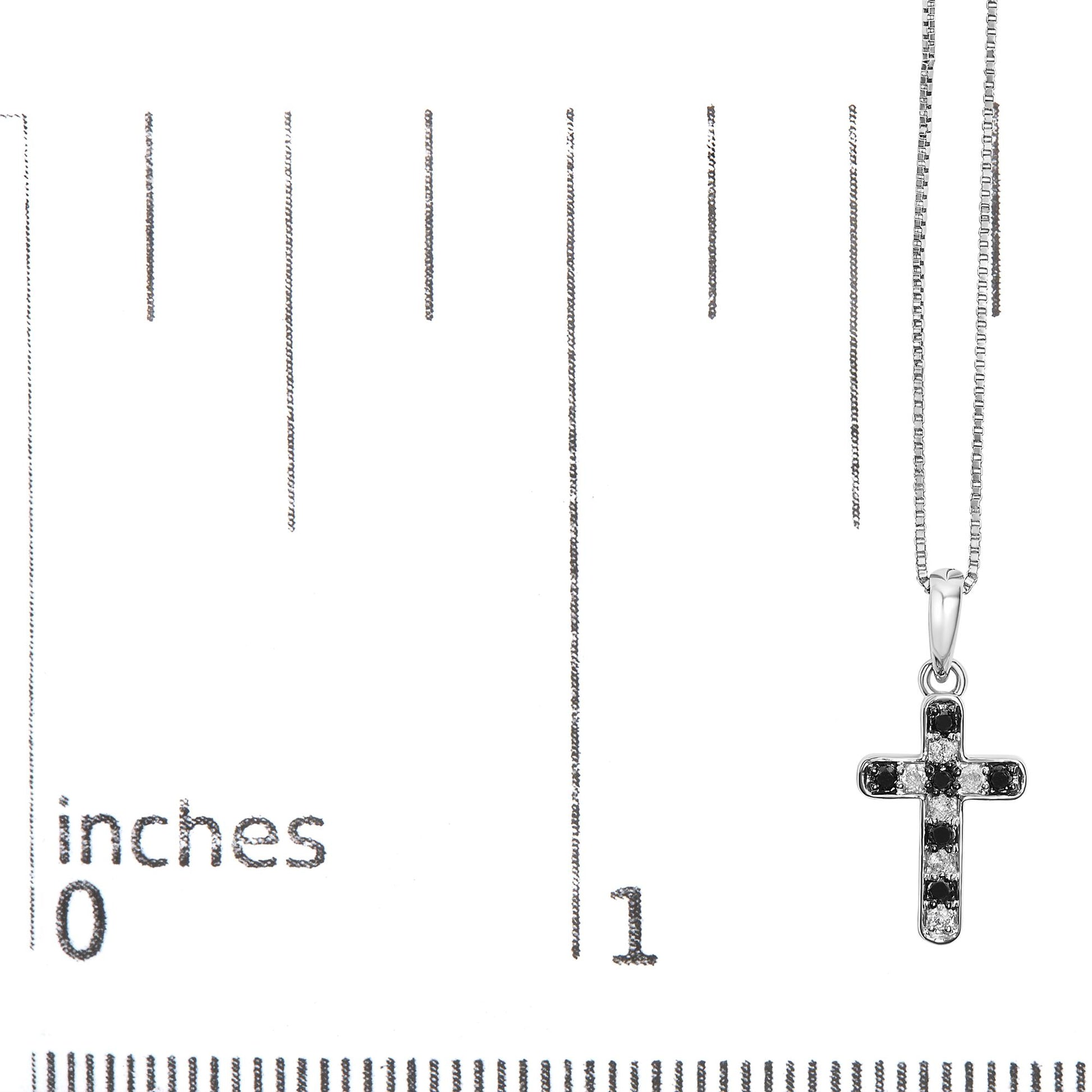 White metal cross-shaped necklace pendant with alternating black and white round gemstones in prong settings, hanging on a white metal chain, shown against a ruler for size reference, front view.