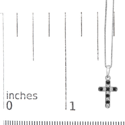 White metal cross-shaped necklace pendant with alternating black and white round gemstones in prong settings, hanging on a white metal chain, shown against a ruler for size reference, front view.