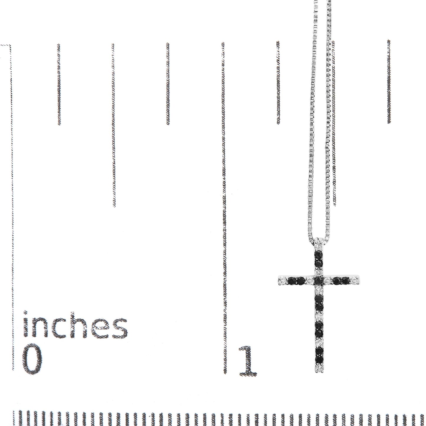 White metal cross-shaped necklace pendant with alternating rows of round black and white gemstones in prong settings, displayed on a ruler for size reference, front view.