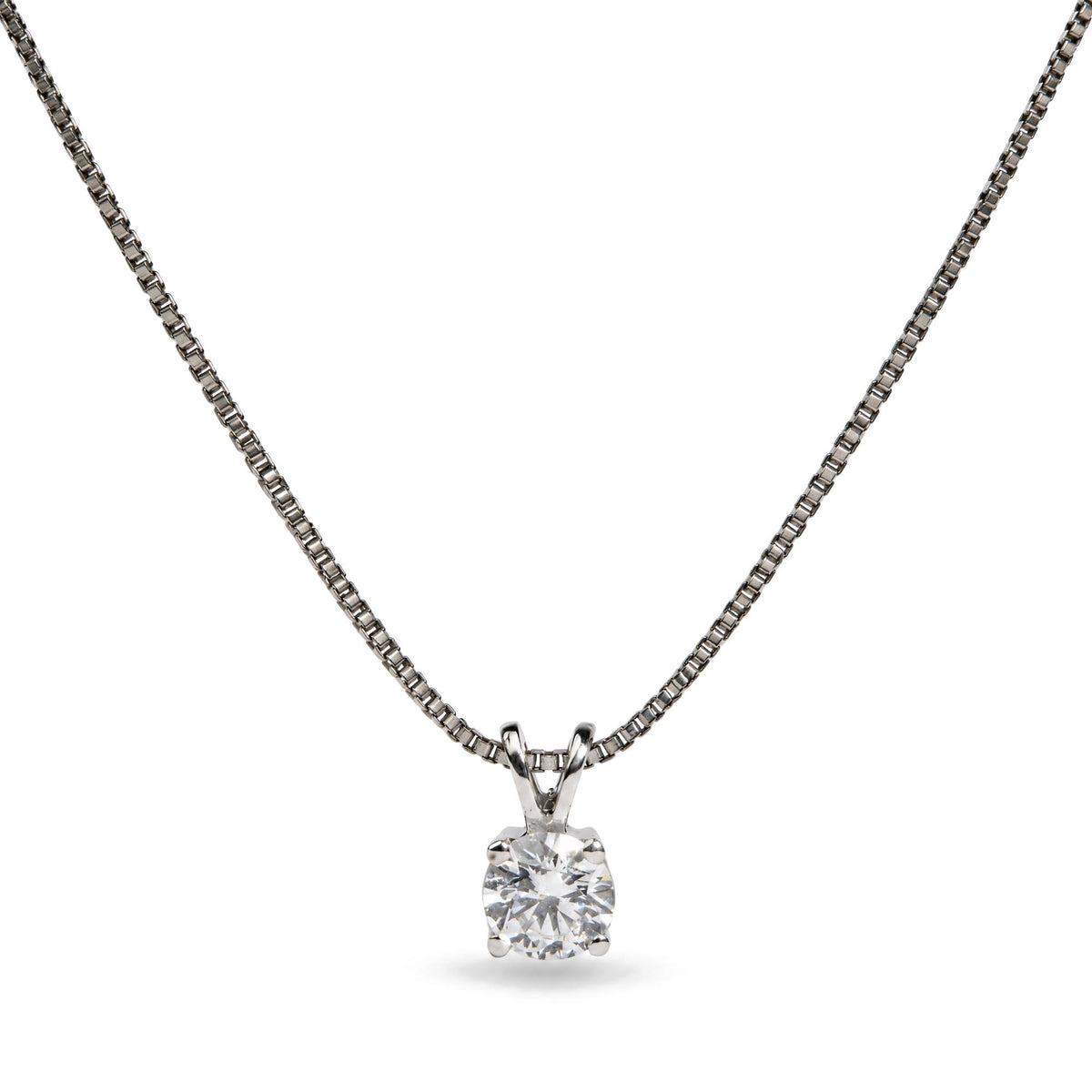 Close-up front view of a white metal necklace with a round white gemstone in a four-prong setting pendant on a chain.