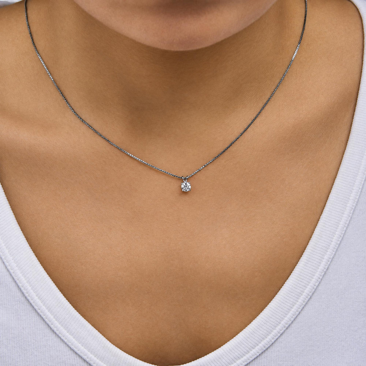 Close-up front angle of a model wearing a white metal necklace with a chain and a single round white gemstone in a four-prong setting pendant.