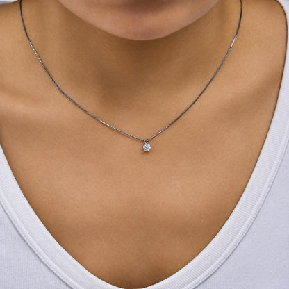 Close-up front angle of a model wearing a white metal necklace with a chain and a single round white gemstone in a four-prong setting pendant.