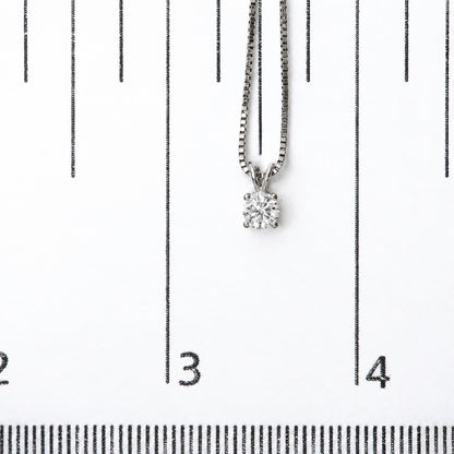 Close-up front view of a white necklace with a round white gemstone in a four-prong setting, shown on a scale with black markings.