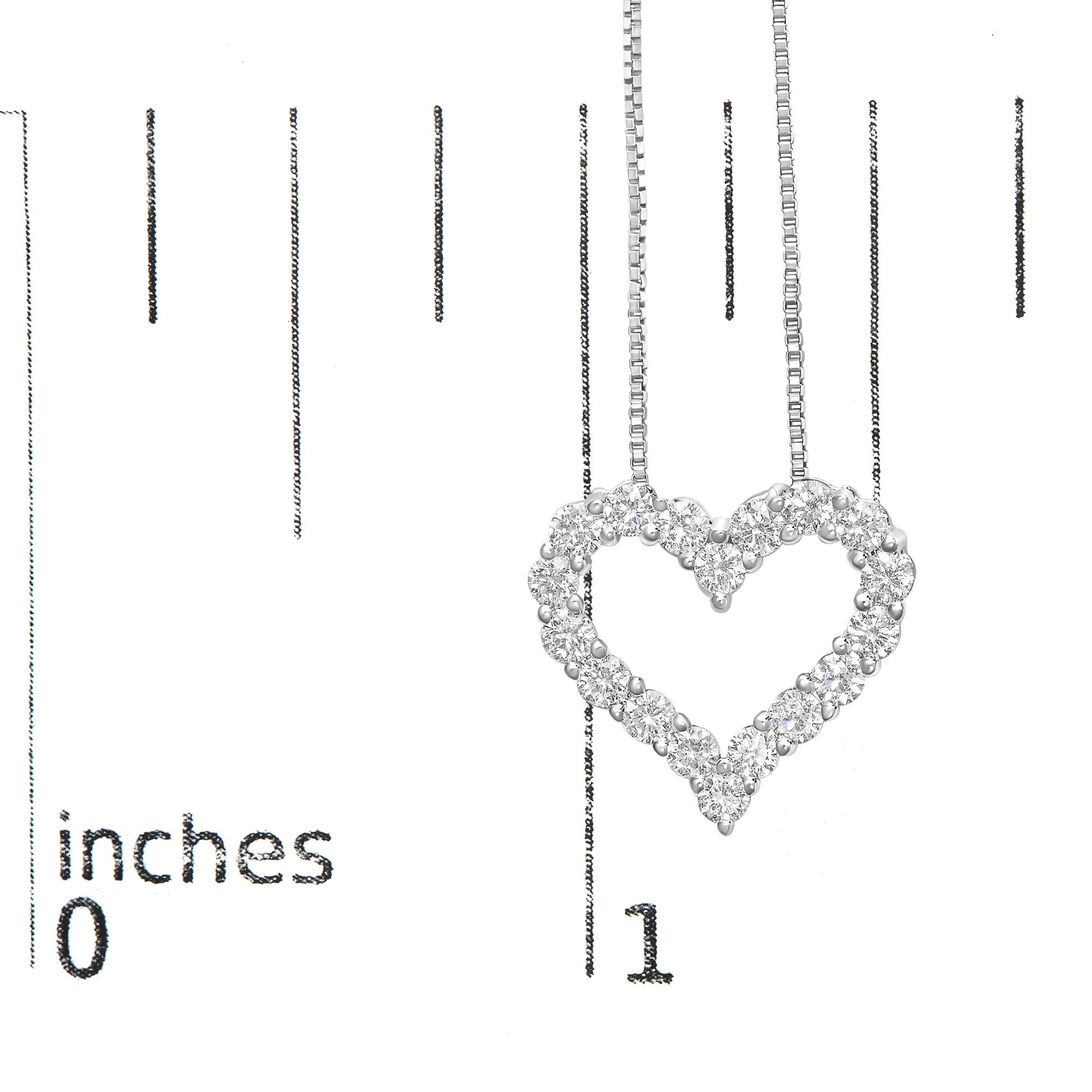 Close-up of a white metal heart-shaped necklace pendant with round white gemstones in prong settings, shown hanging against a ruler for size reference.