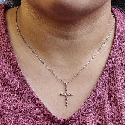 Close-up front view of a necklace on a model featuring a white metal cross pendant adorned with round black and white gemstones in prong settings on a thin chain.