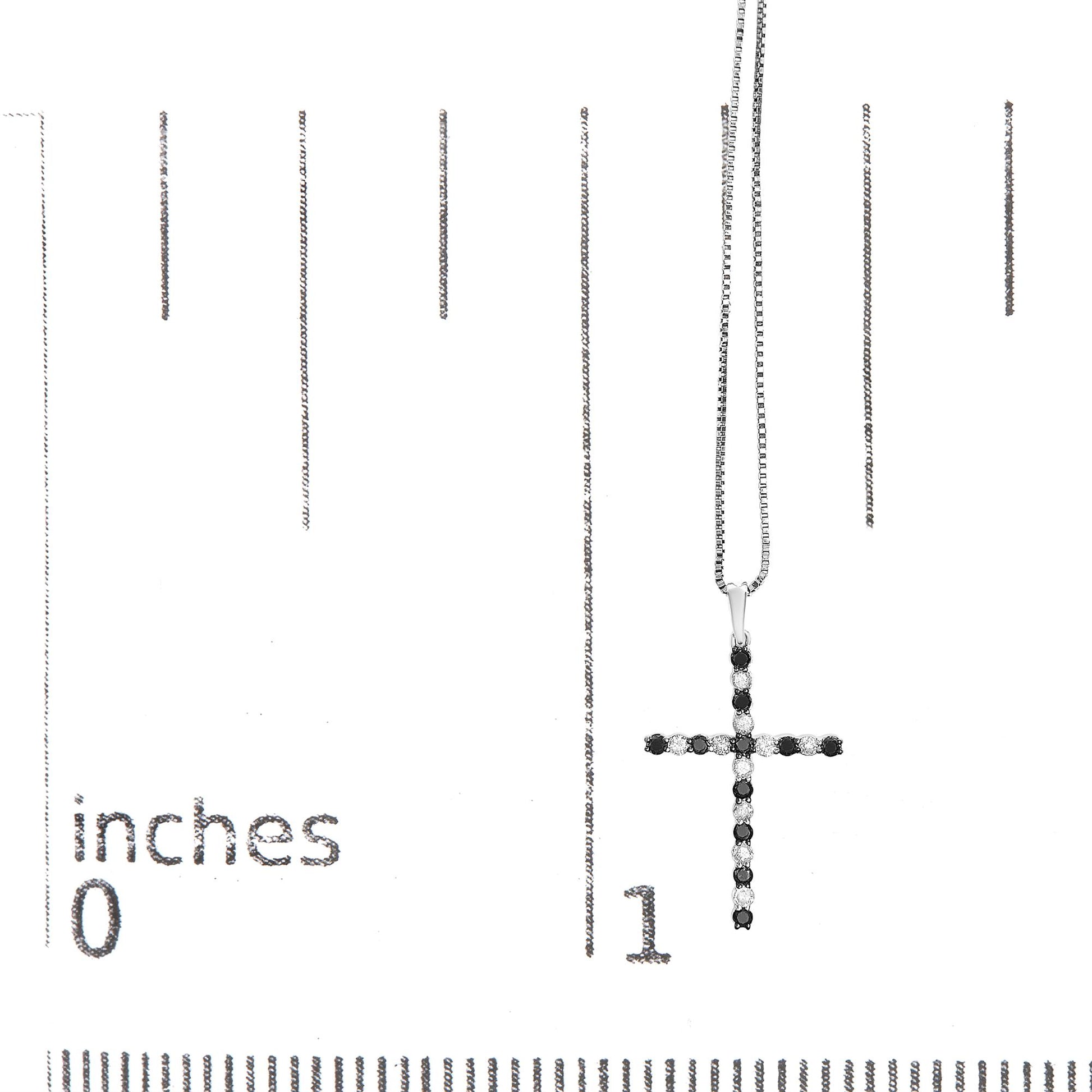 White metal cross necklace with alternating black and white round gemstones in prong settings, shown hanging on a ruler for size reference, front-facing angle.