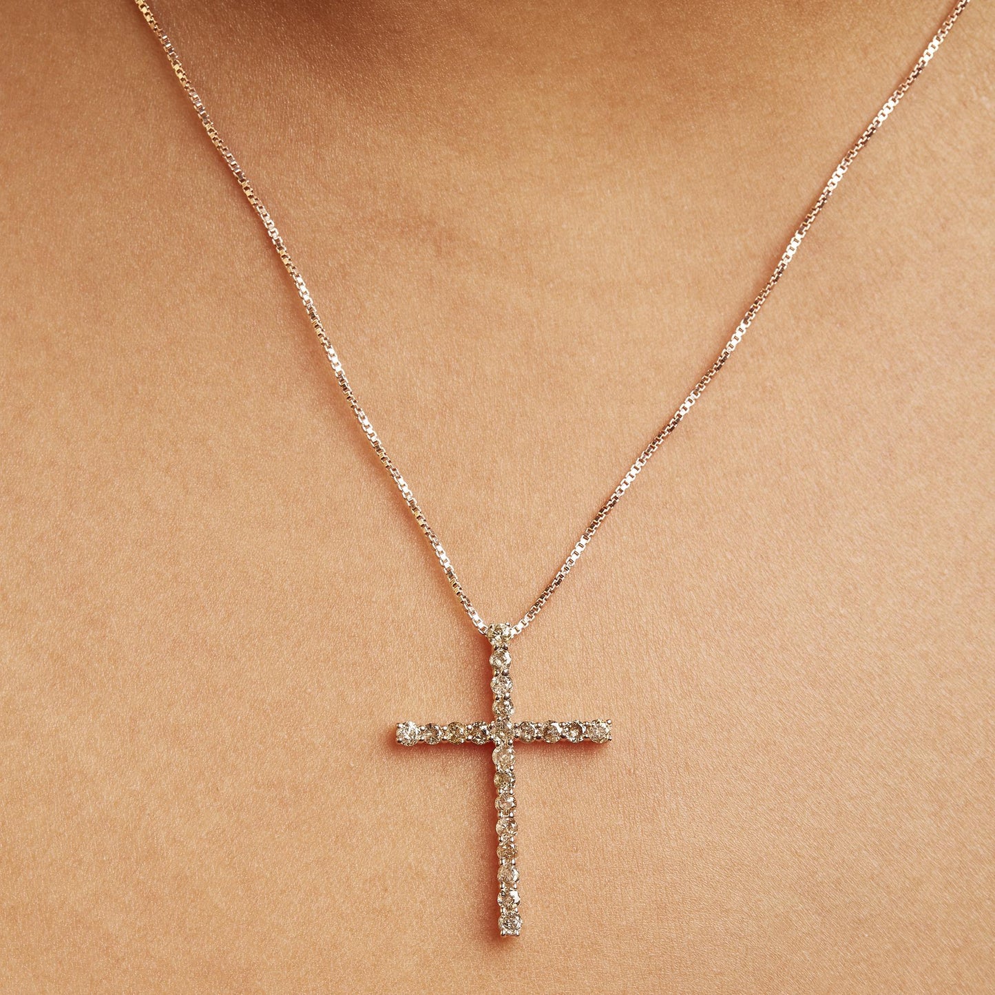 Rose metal necklace with a cross pendant featuring round champagne-colored gemstones in prong settings, shown on a model from a front close-up angle.