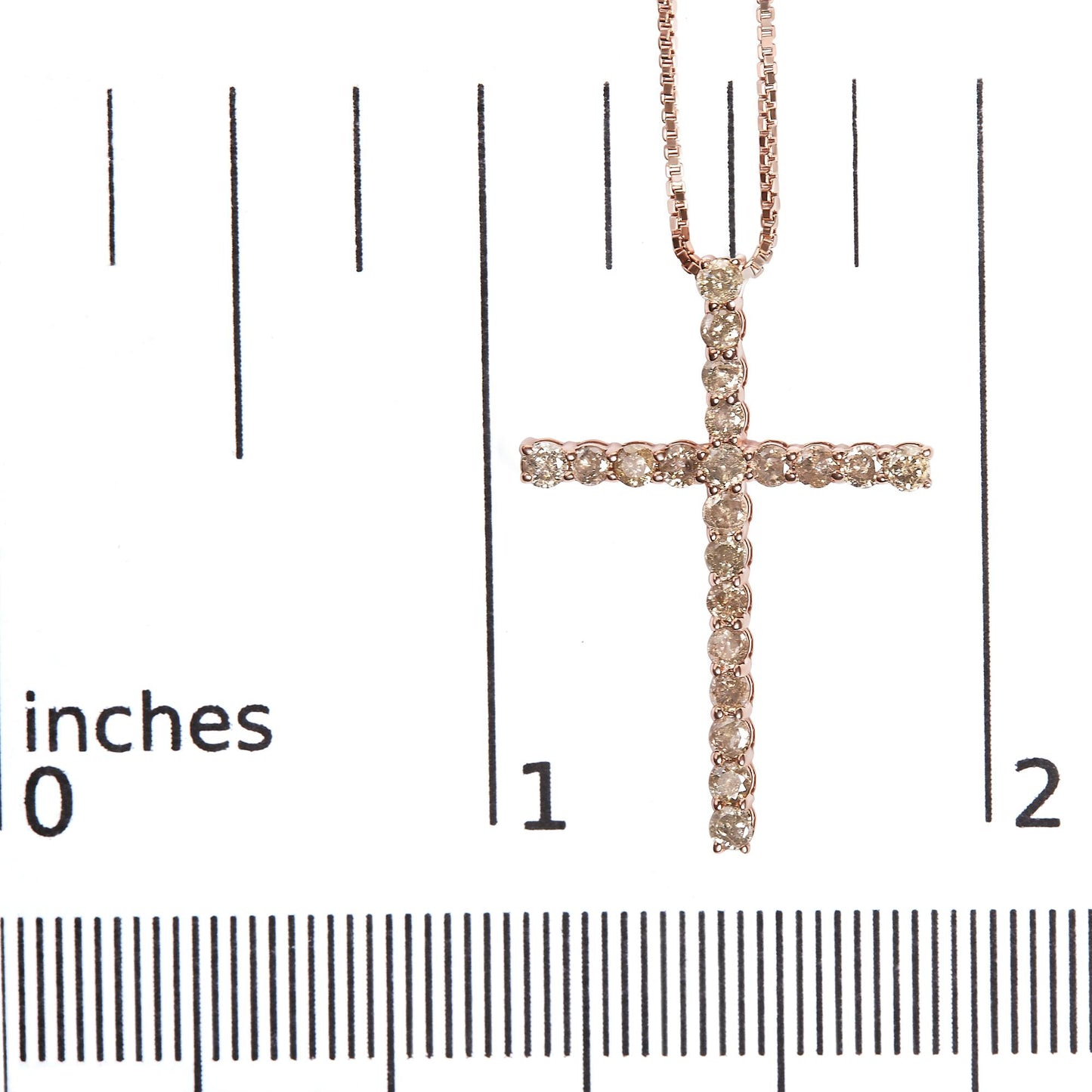 Close-up front view of a rose-colored metal cross necklace pendant set with round champagne-colored gemstones in prong settings, placed on a ruler for size reference.