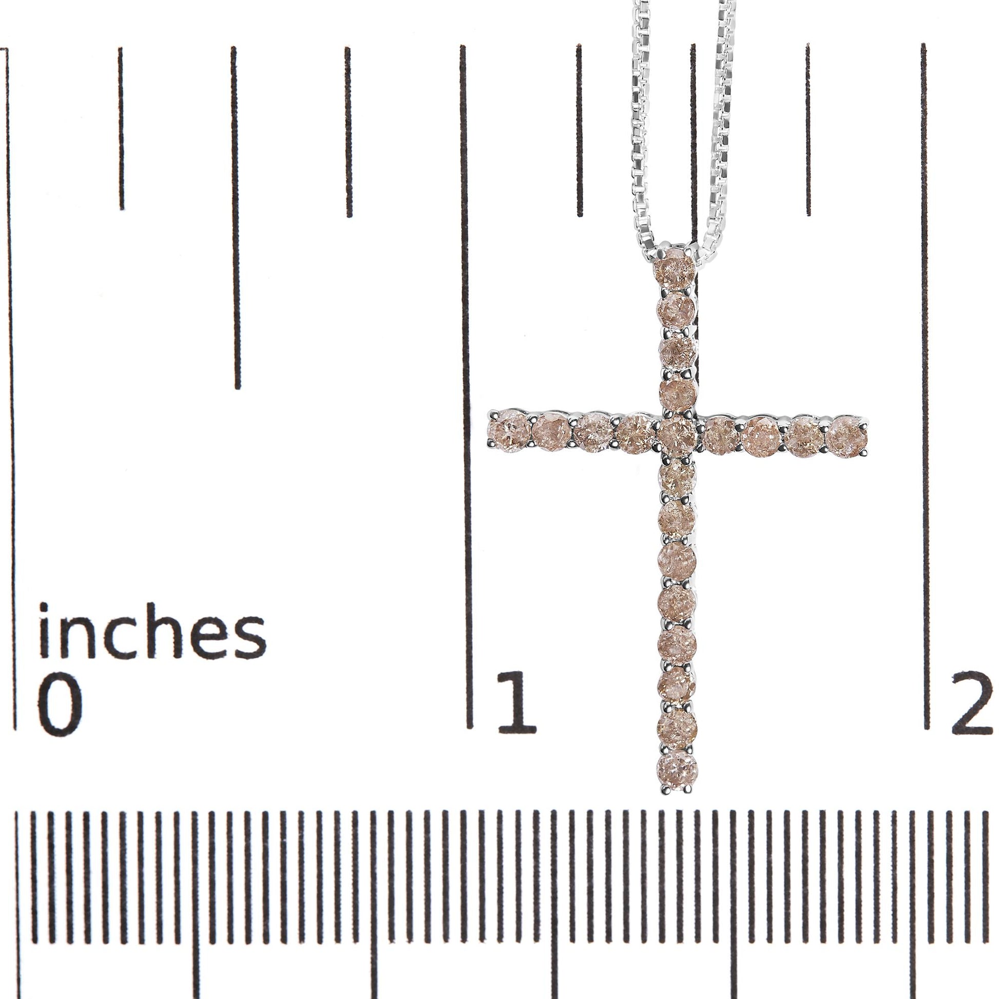 Close-up front view of a white metal cross necklace pendant with round champagne-colored gemstones in prong settings, shown on a ruler for size reference.