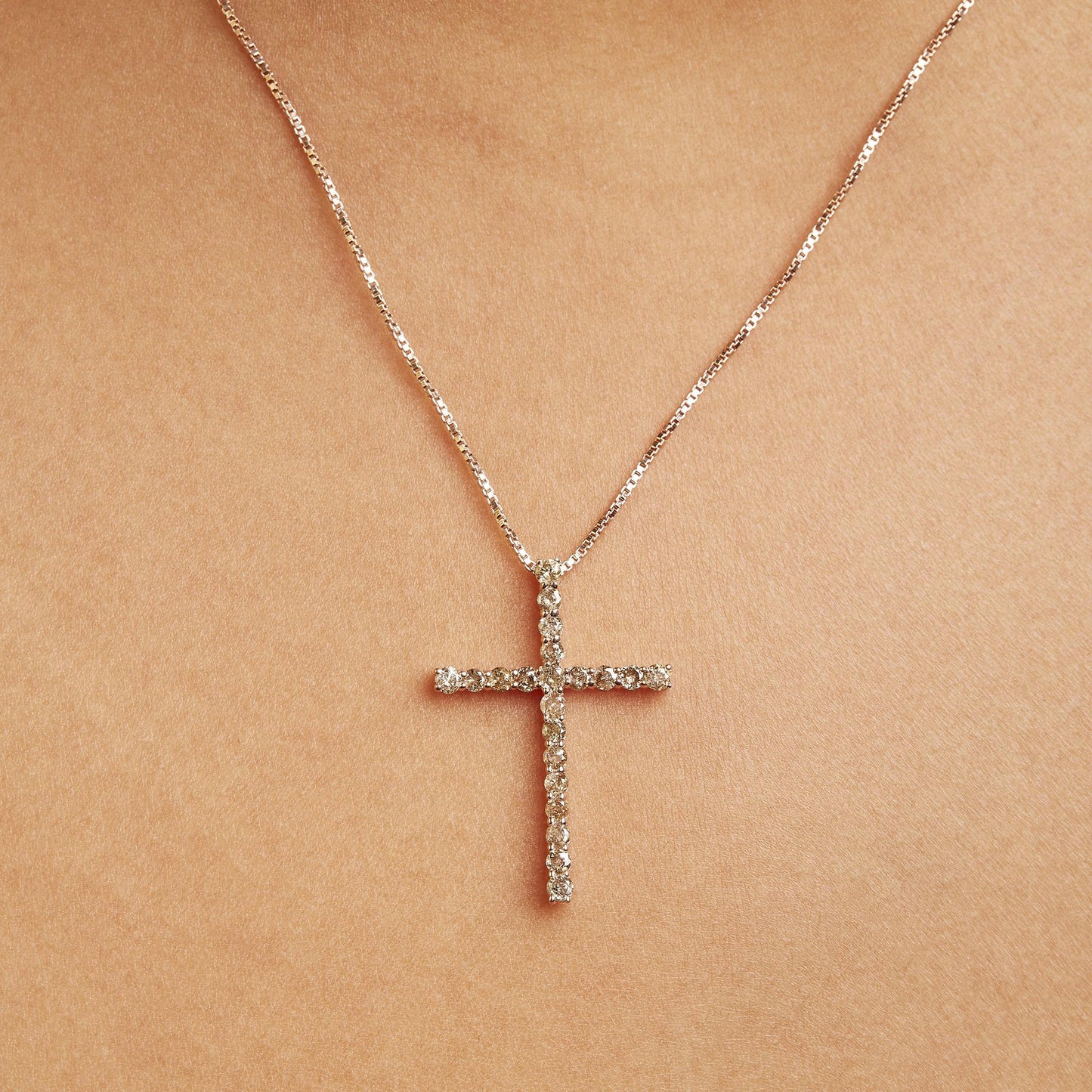 Close-up front view of a yellow metal necklace on a model featuring a cross-shaped pendant adorned with round brownish gemstones in prong settings.