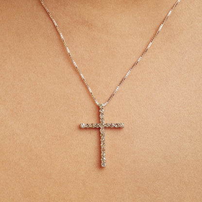 Close-up front view of a yellow metal necklace on a model featuring a cross-shaped pendant adorned with round brownish gemstones in prong settings.
