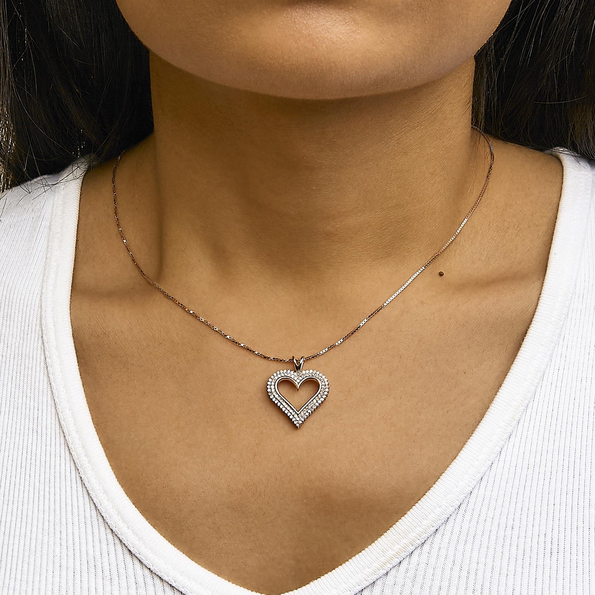 Close-up front view of a rose-colored necklace with a heart-shaped pendant adorned with round white gemstones, worn on a model.
