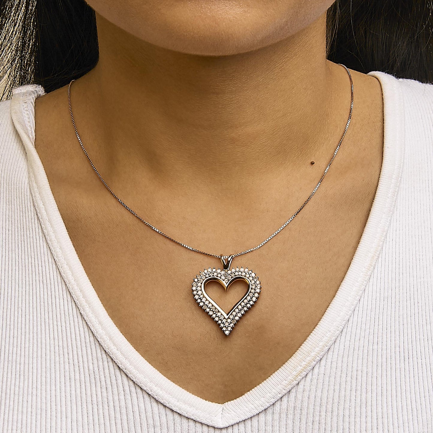 Rose metal heart-shaped necklace pendant with prong-set round white gemstones, worn on a model, front view.