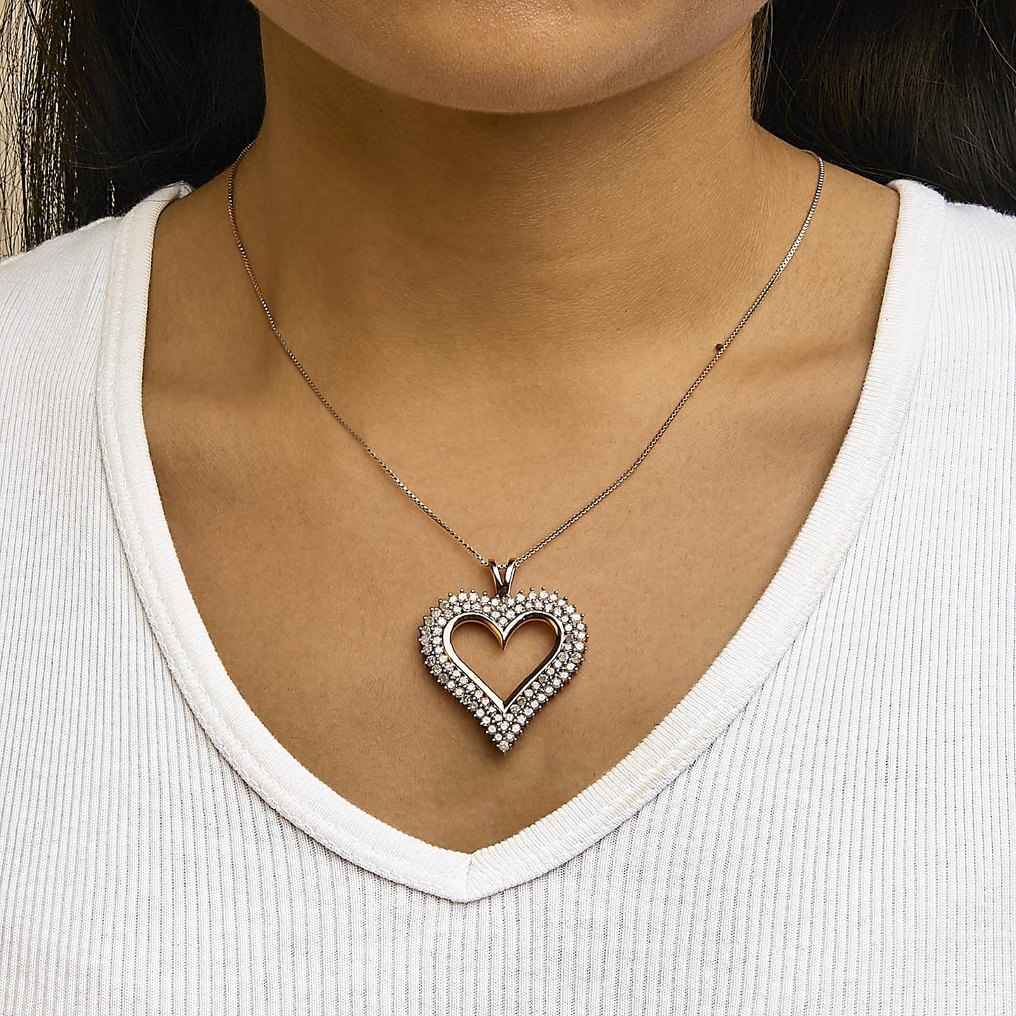 Close-up front view of a rose-colored necklace with a heart-shaped pendant adorned with round white gemstones, worn on a model.