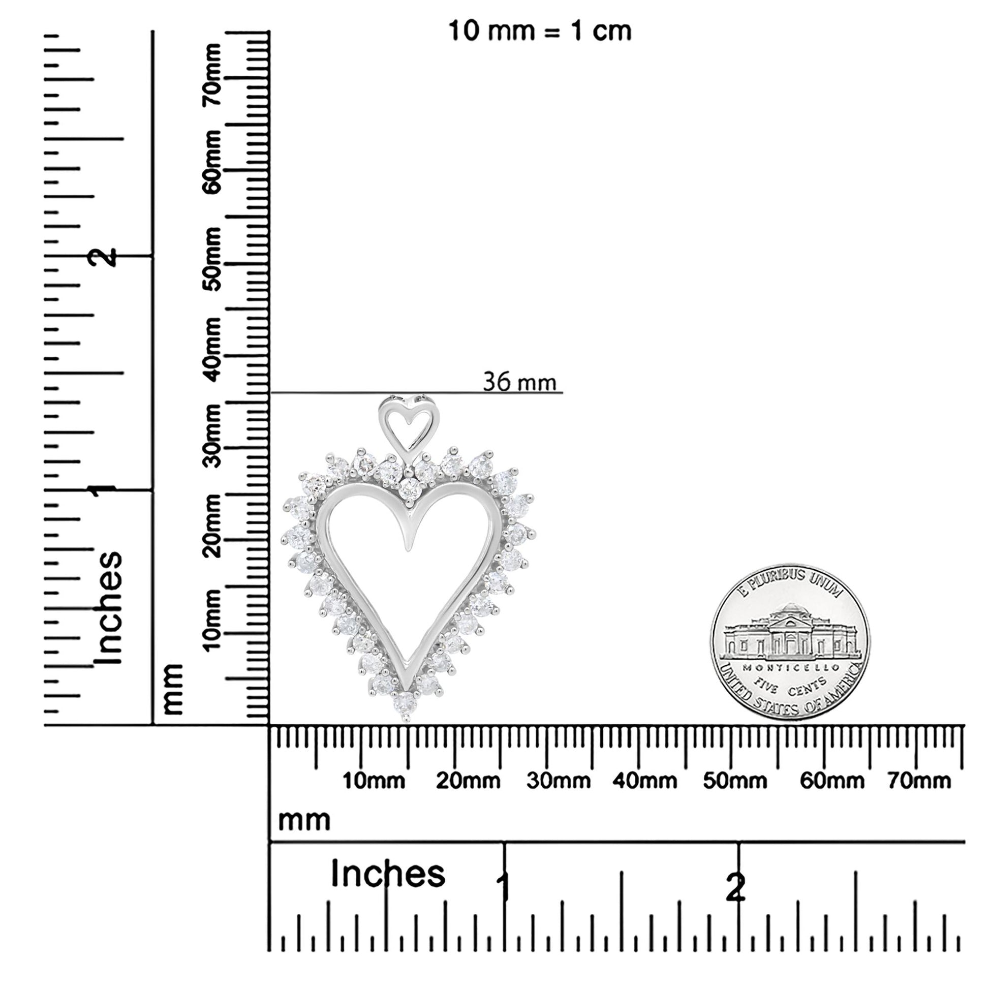 Top-down view of a white metal heart-shaped necklace pendant with a smaller heart at the top, surrounded by round white gemstones in prong settings, placed on a ruler for size reference.