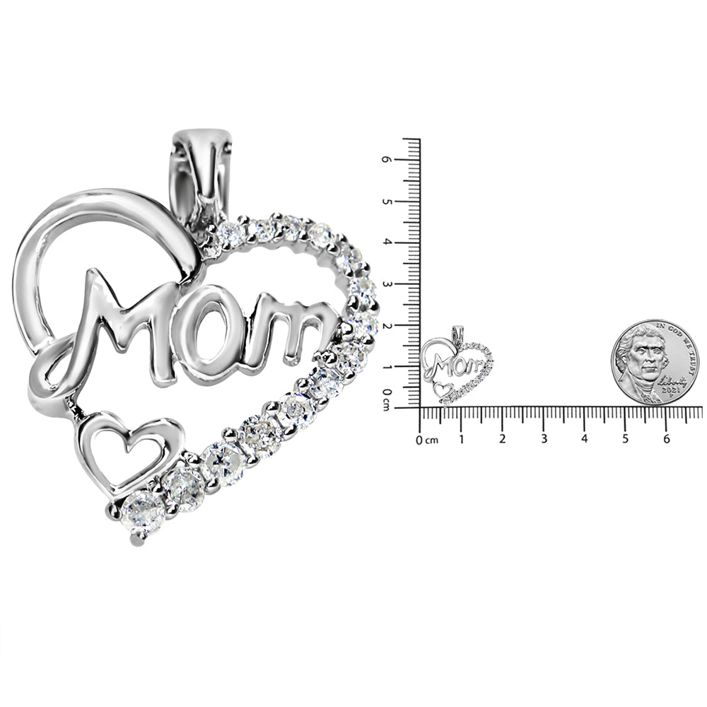 Close-up front angle of a white metal heart-shaped necklace pendant with the word 'Mom' inside, adorned with prong-set white round gemstones along the heart outline, shown next to a ruler and a coin for size reference.