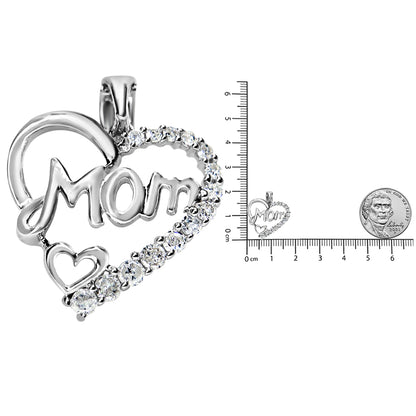 Close-up front angle of a white metal heart-shaped necklace pendant with the word 'Mom' inside, adorned with prong-set white round gemstones along the heart outline, shown next to a ruler and a coin for size reference.