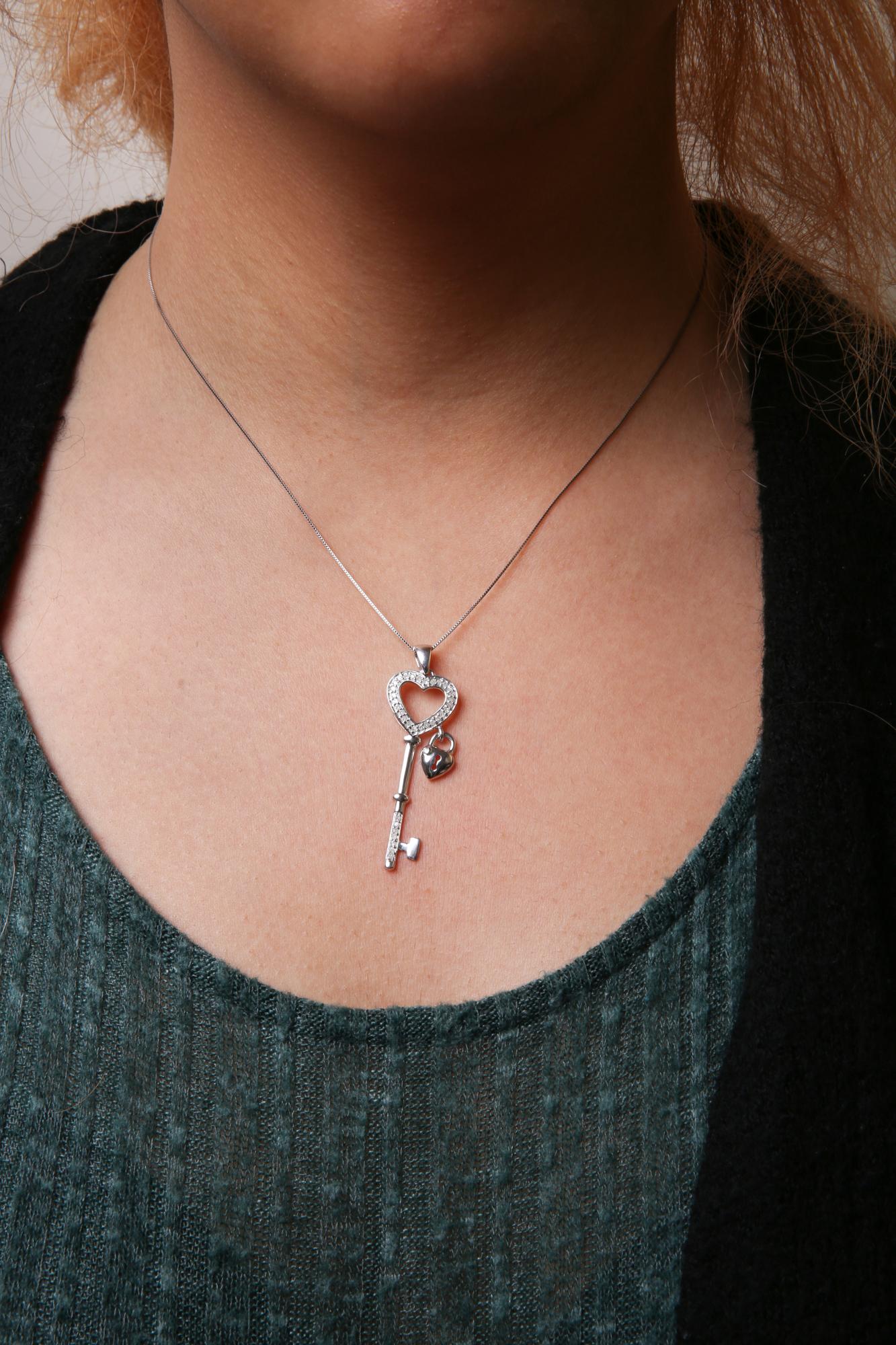 White metal necklace with a heart-shaped key pendant adorned with white gemstones, shown on a model from a front angle.