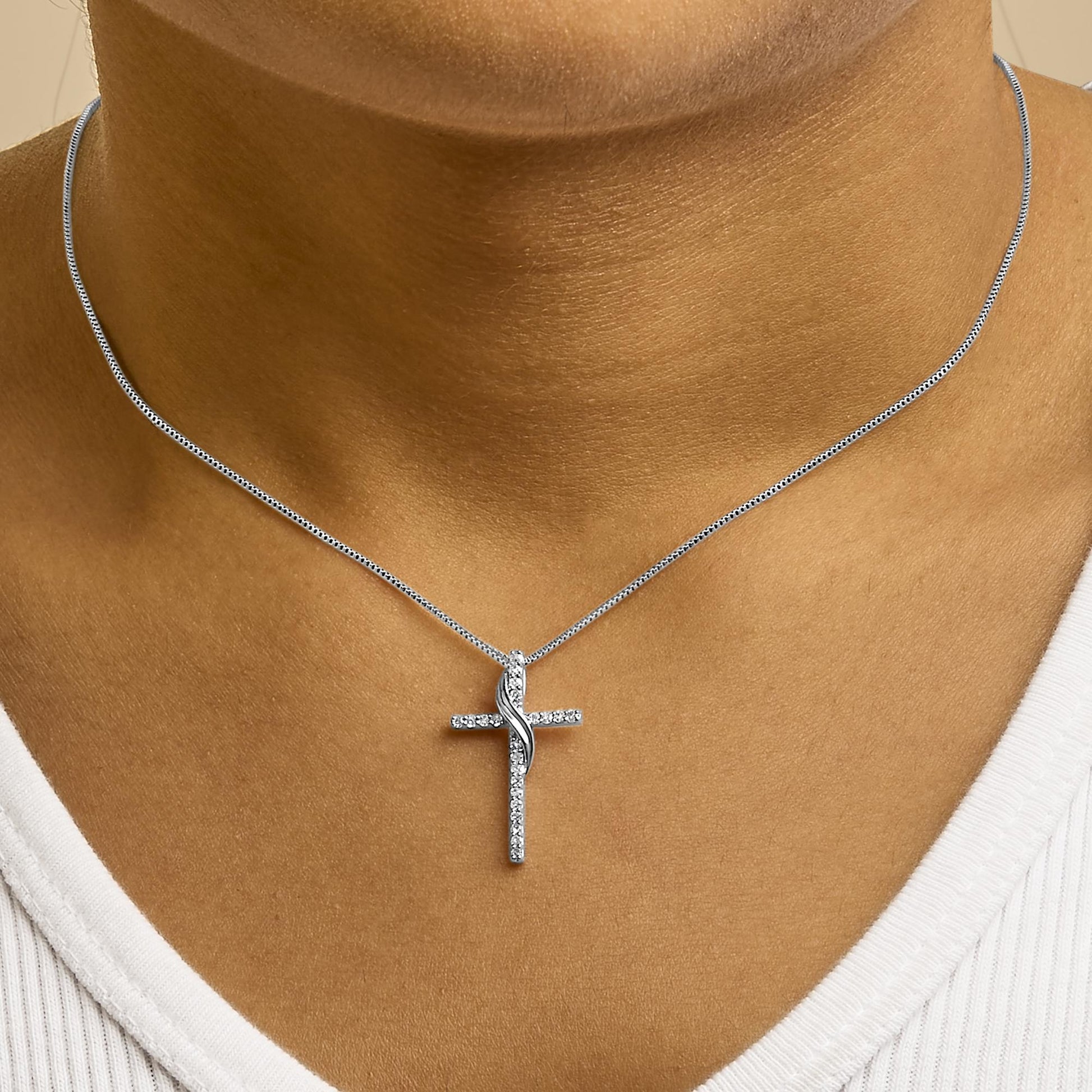 Close-up front view of a white metal necklace on a model's neck featuring a cross pendant adorned with round white gemstones in prong settings.