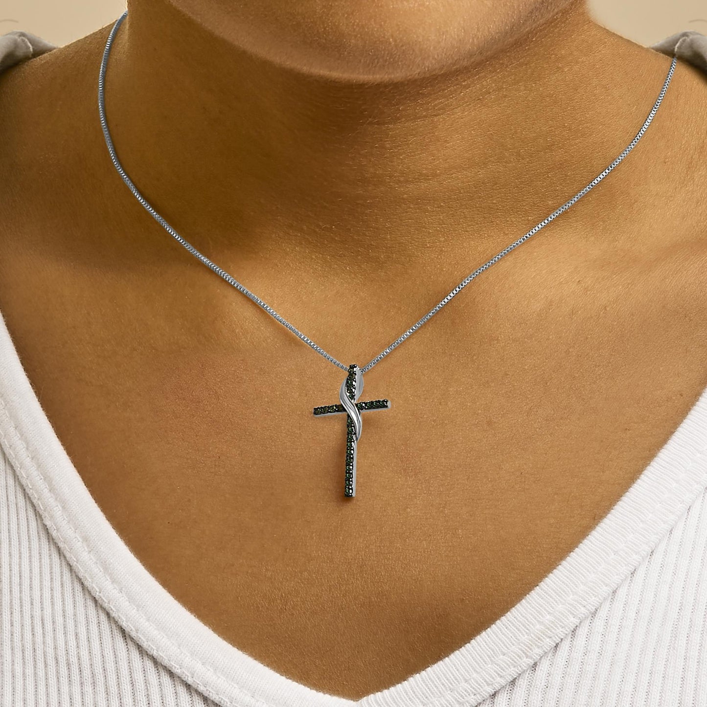 Close-up front view of a white metal necklace with a cross pendant adorned with blue round gemstones in prong settings, worn on a model.