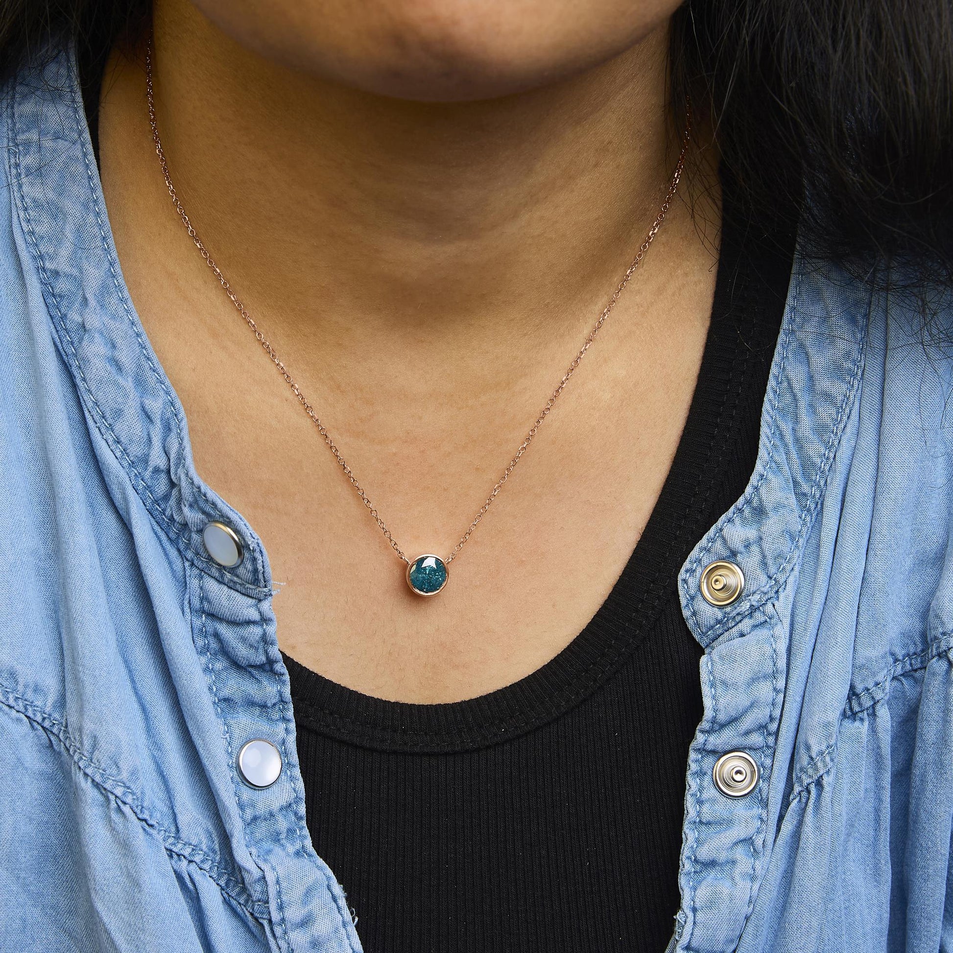 Rose metal necklace with a round blue gemstone in bezel setting, shown worn by a model in a close-up front view.