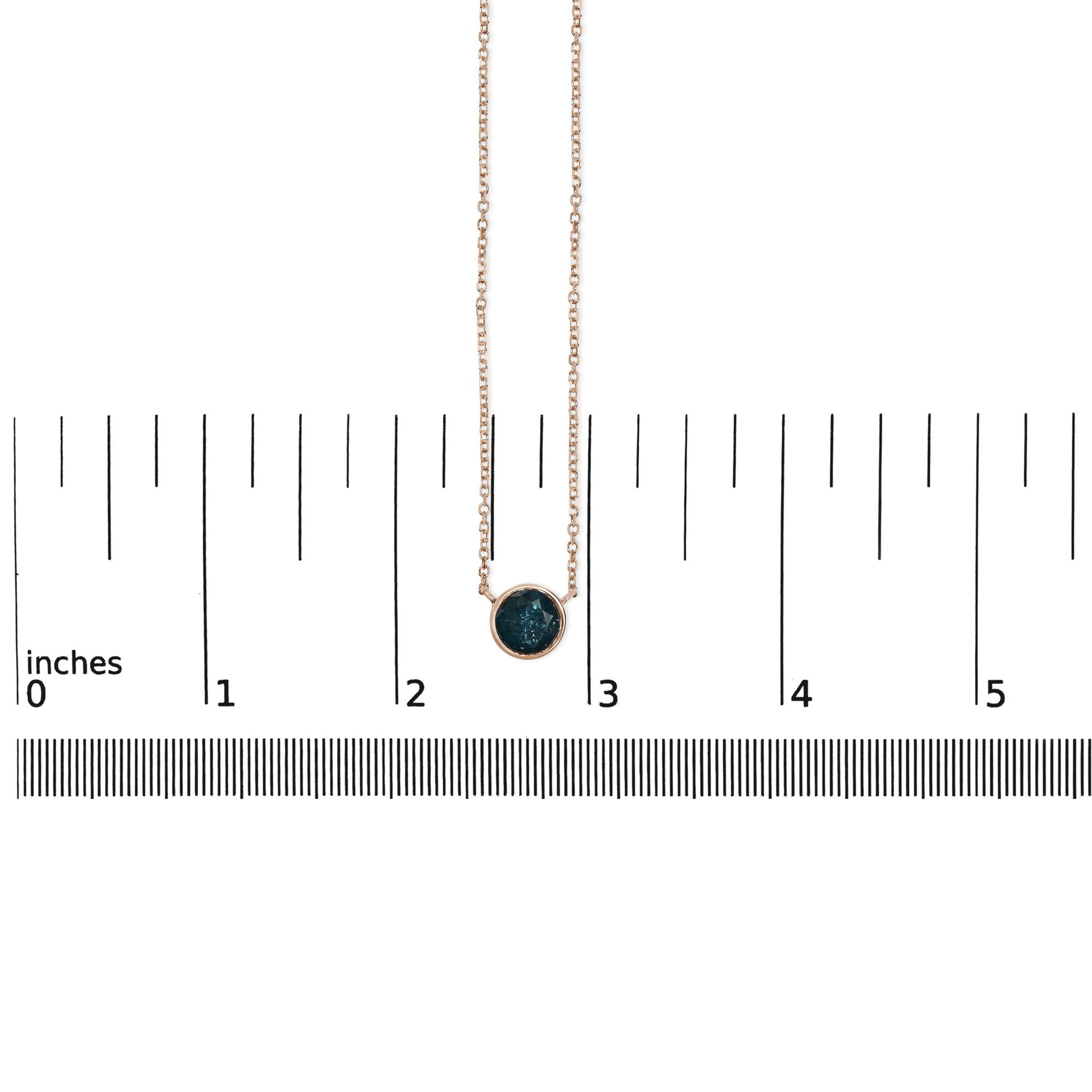 Rose metal necklace with a round blue gemstone in bezel setting, shown hanging vertically on a scale with measurement markings, front view.