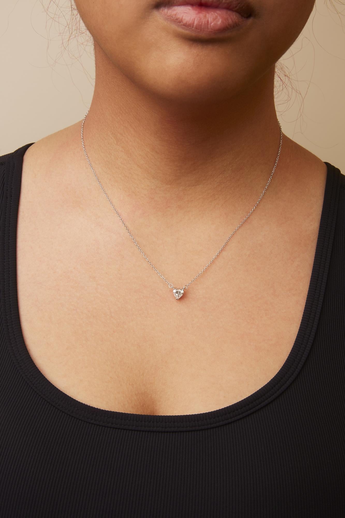 White metal necklace with a heart-shaped white gemstone in a 3-prong setting, shown worn on a model from a front angle.