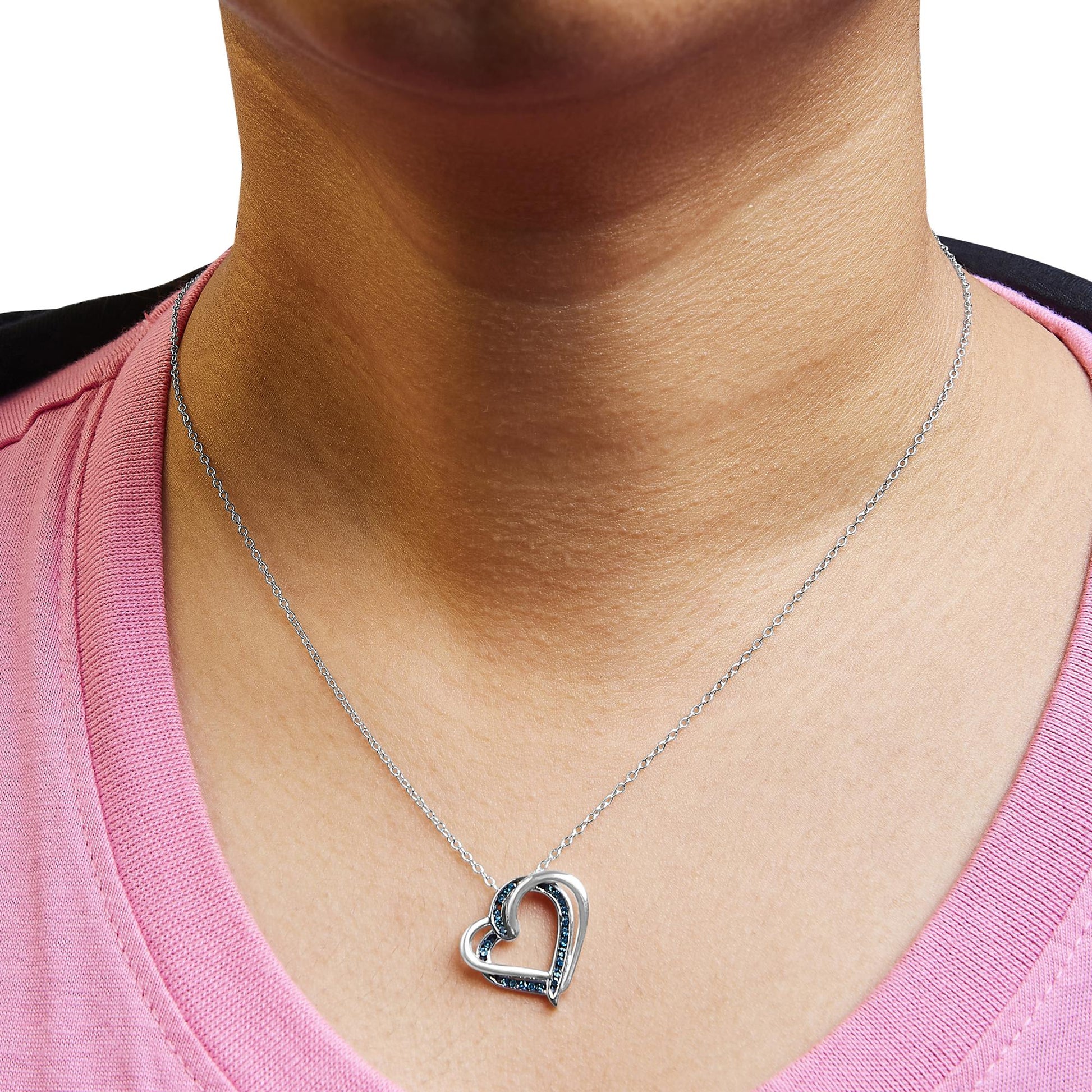 White metal heart-shaped necklace with channel-set round blue gemstones, worn on a model, front-facing angle.