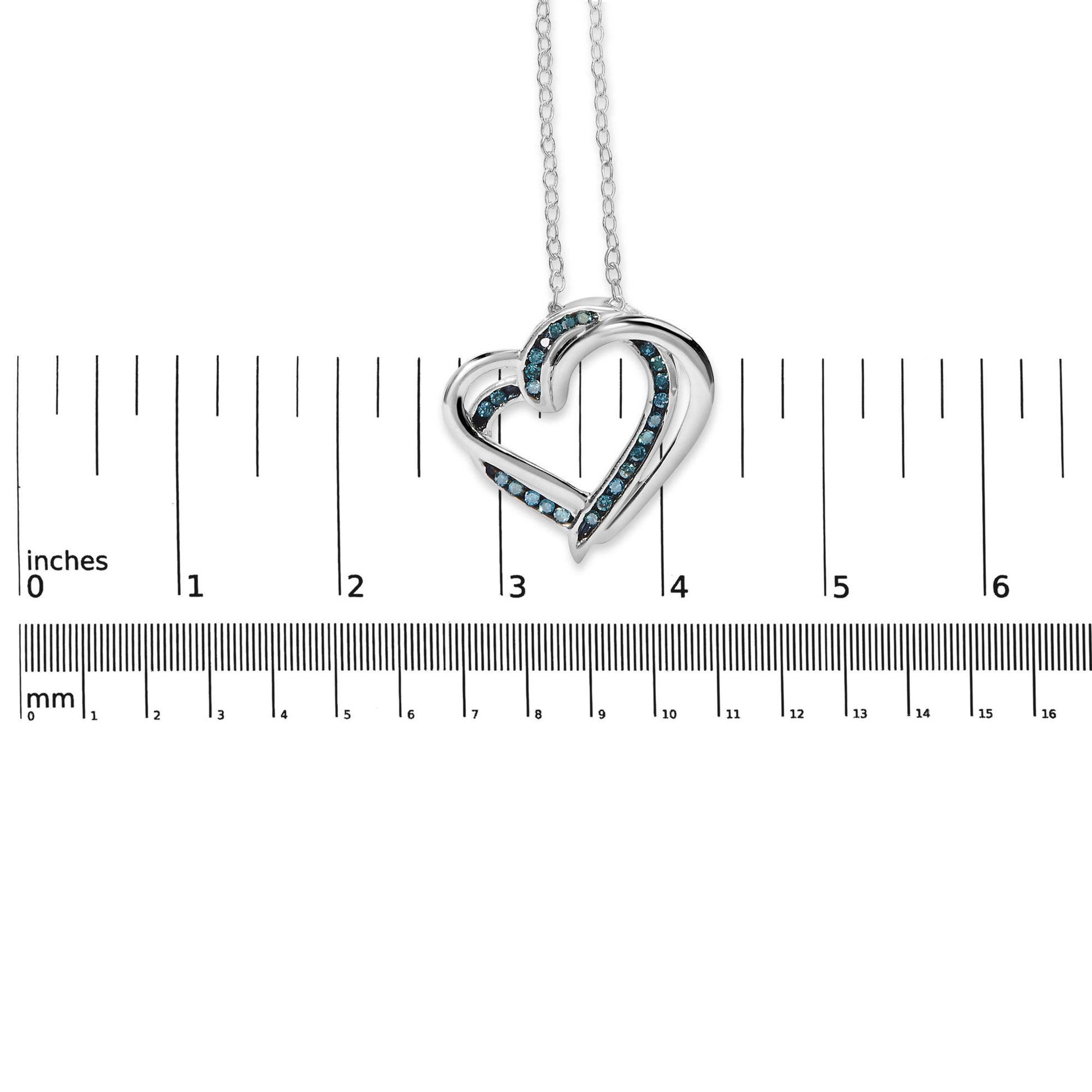 White metal necklace with heart-shaped pendant featuring blue round gemstones in channel setting, shown on a ruler for size reference, front view.