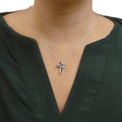 White metal necklace with cross-shaped pendant featuring prong-set round blue gemstones, shown on a model from front angle.