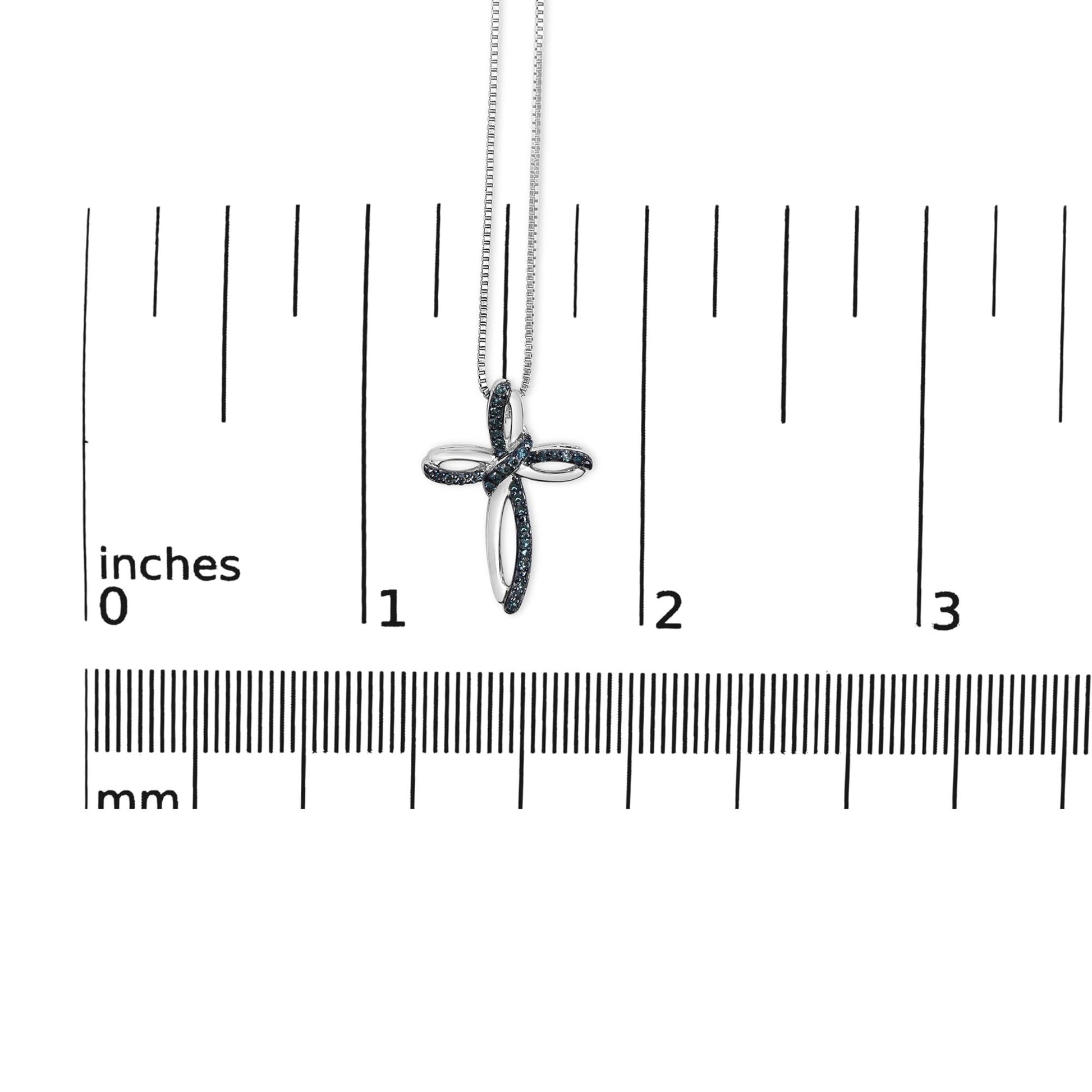 White metal necklace with a cross pendant featuring blue round gemstones in prong settings, hanging against a ruler for size reference, front view.