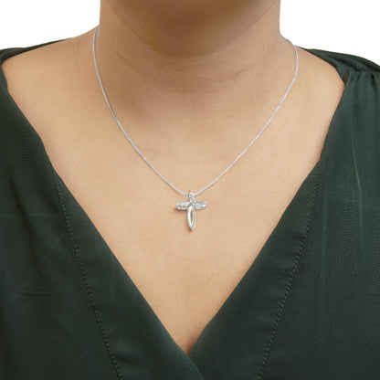 Close-up front view of a white metal cross-shaped necklace with small yellow round gemstones in prong settings, worn on a model with a dark green top.