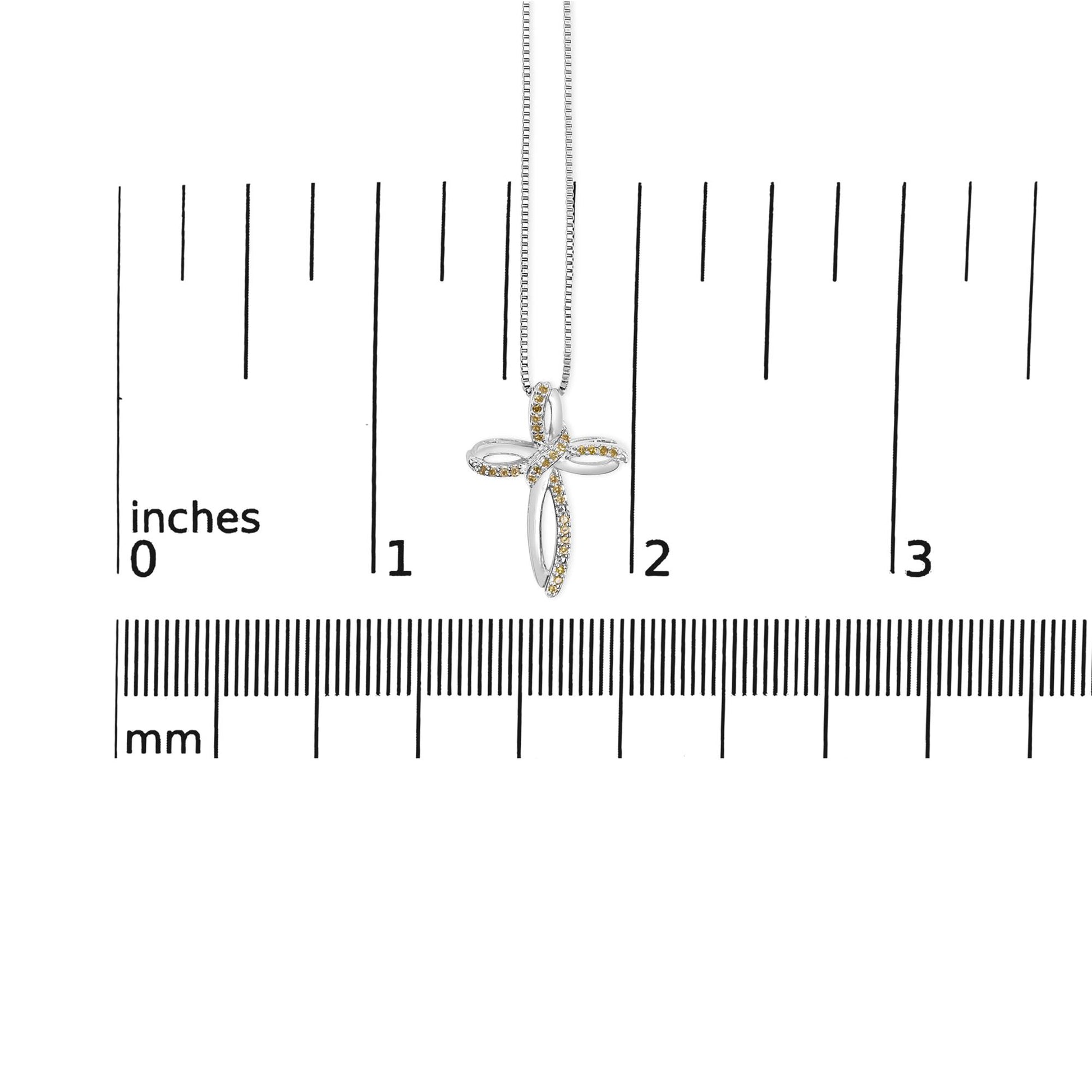 White metal cross-shaped necklace pendant with small yellow gemstones in prong settings, shown front-facing on a ruler for size reference.