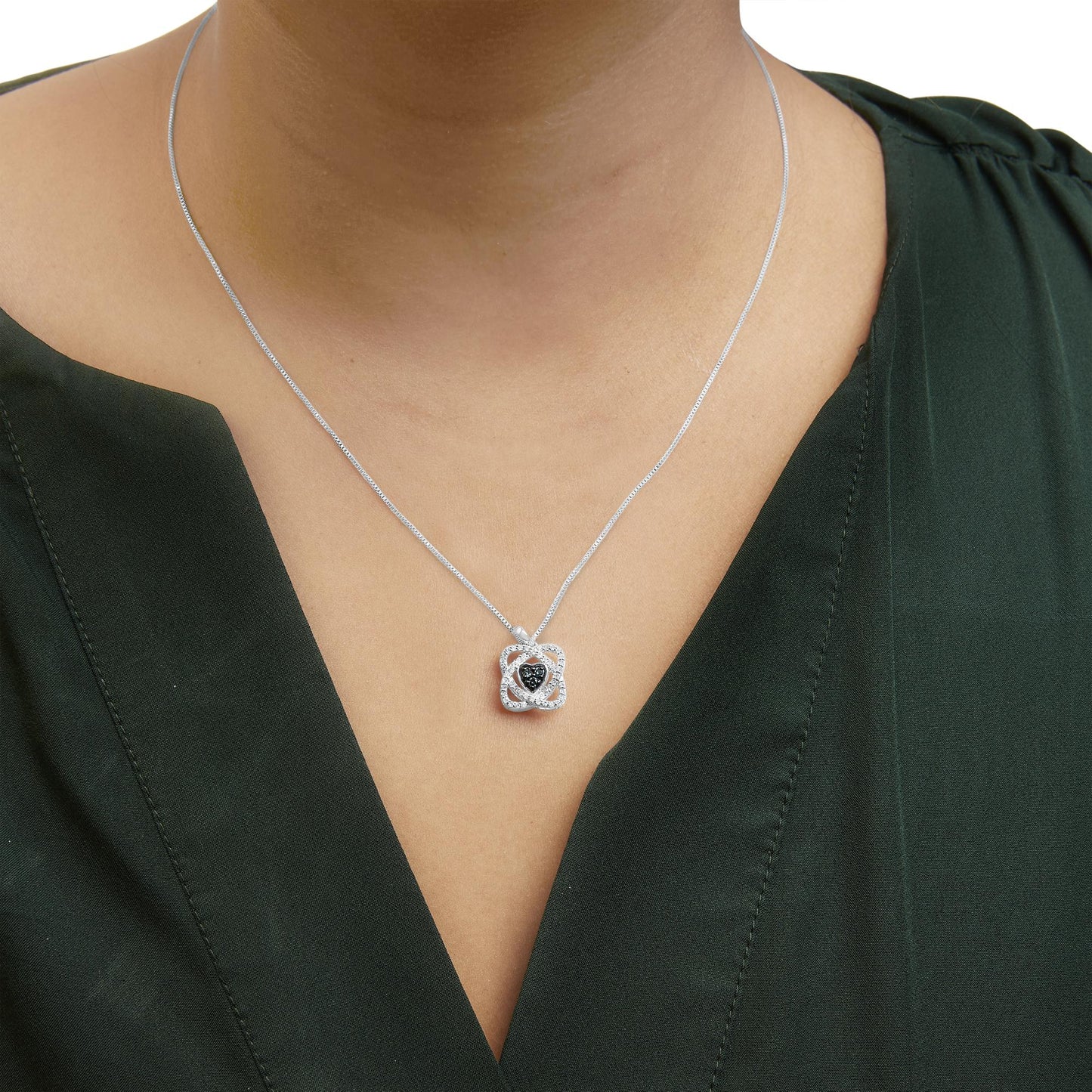 Close-up front view of a white metal necklace with a flower-shaped pendant featuring three blue round gemstones in the center and surrounded by multiple small white round gemstones, worn on a model in a dark green top.
