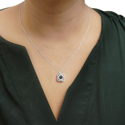 Close-up front view of a white metal necklace with a flower-shaped pendant featuring three blue round gemstones in the center and surrounded by multiple small white round gemstones, worn on a model in a dark green top.