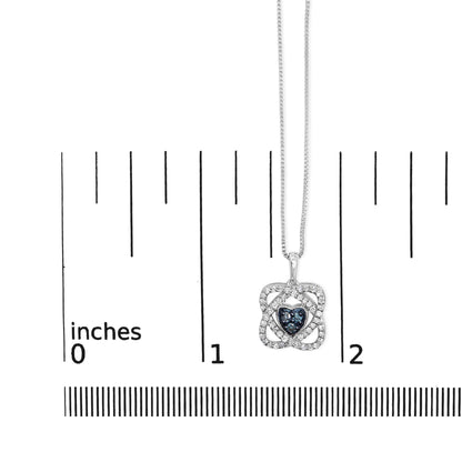 Close-up front view of a white metal necklace pendant on a ruler for size reference, featuring a heart-shaped cluster of blue round gemstones surrounded by a square frame of white round gemstones in prong settings.