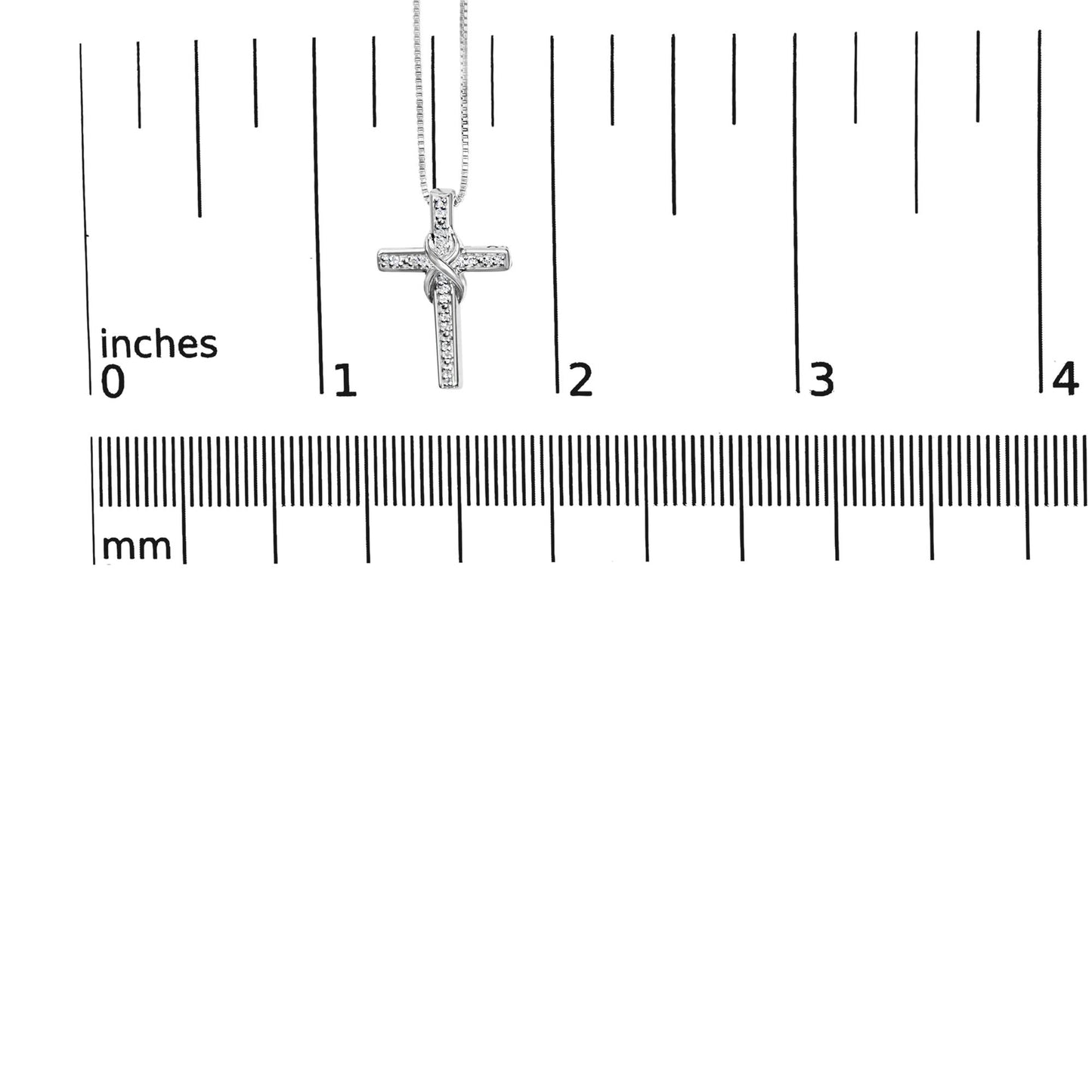 Close-up front view of white metal cross necklace pendant with round prong-set white gemstones, displayed on a ruler for size reference.