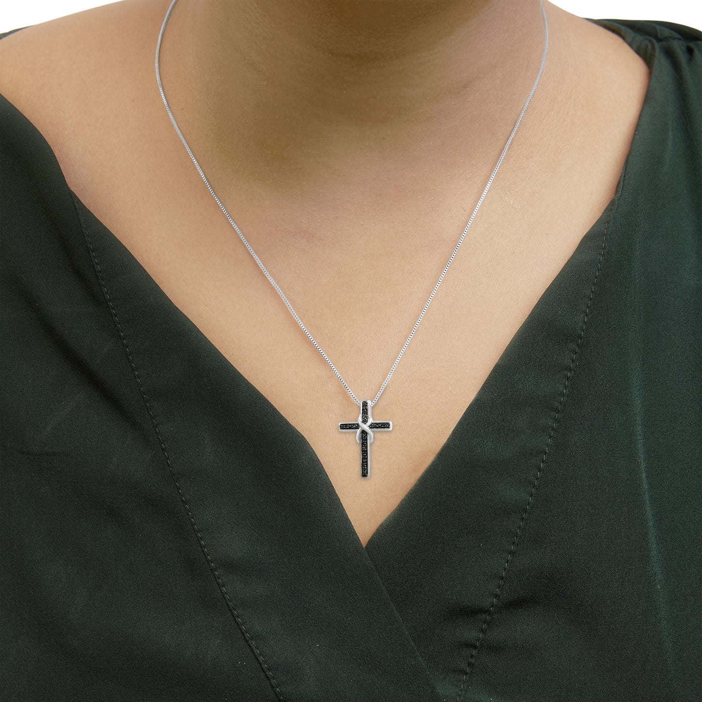 Close-up front view of a white metal necklace with a cross pendant featuring round blue gemstones, worn on a model wearing a dark green top.