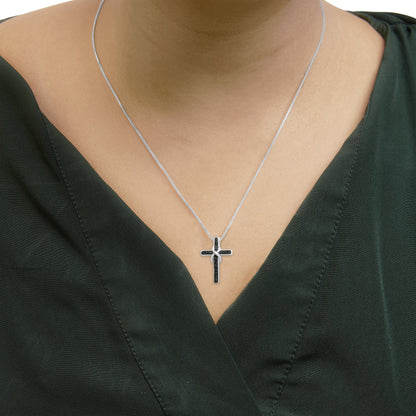 Close-up front view of a white metal necklace with a cross pendant featuring round blue gemstones, worn on a model wearing a dark green top.