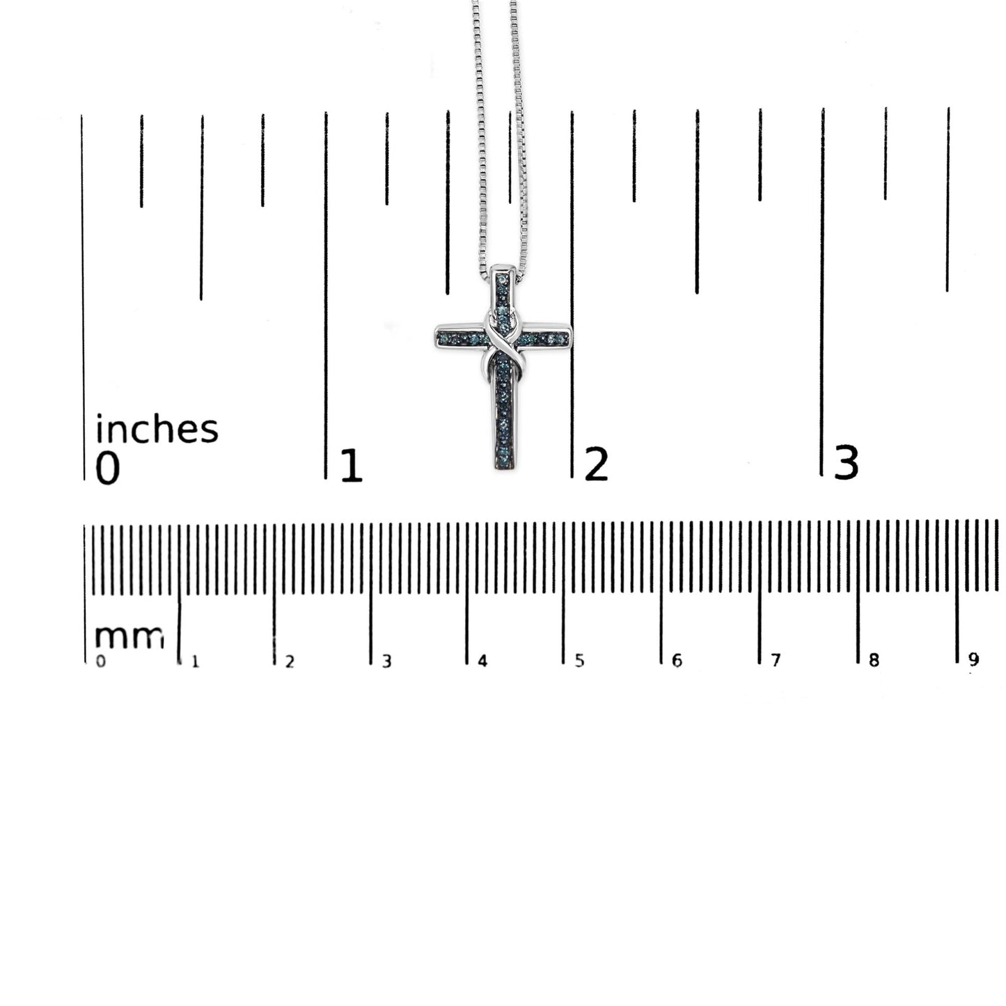 Close-up front view of a white necklace with a cross-shaped pendant adorned with round blue gemstones in a prong setting, displayed on a ruler for size reference.