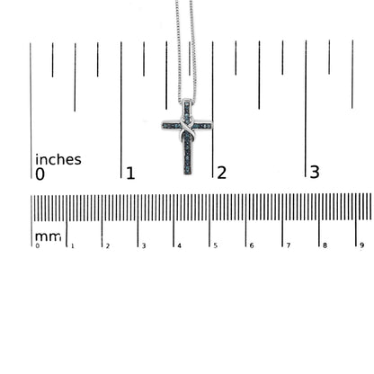 Close-up front view of a white necklace with a cross-shaped pendant adorned with round blue gemstones in a prong setting, displayed on a ruler for size reference.