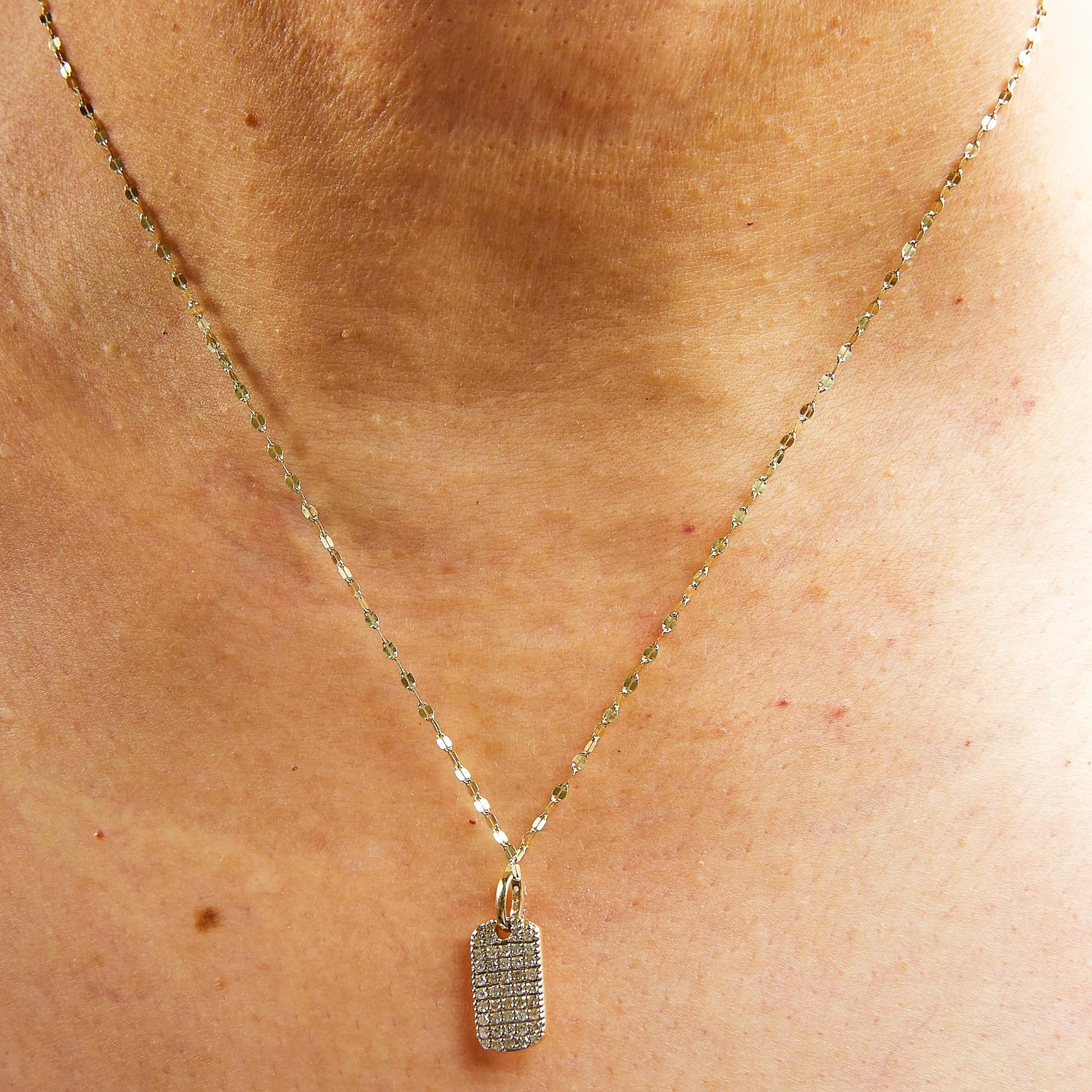 Close-up front view of a yellow metal necklace with a rectangular pendant encrusted with multiple rows of round white gemstones in prong settings, worn on a model.