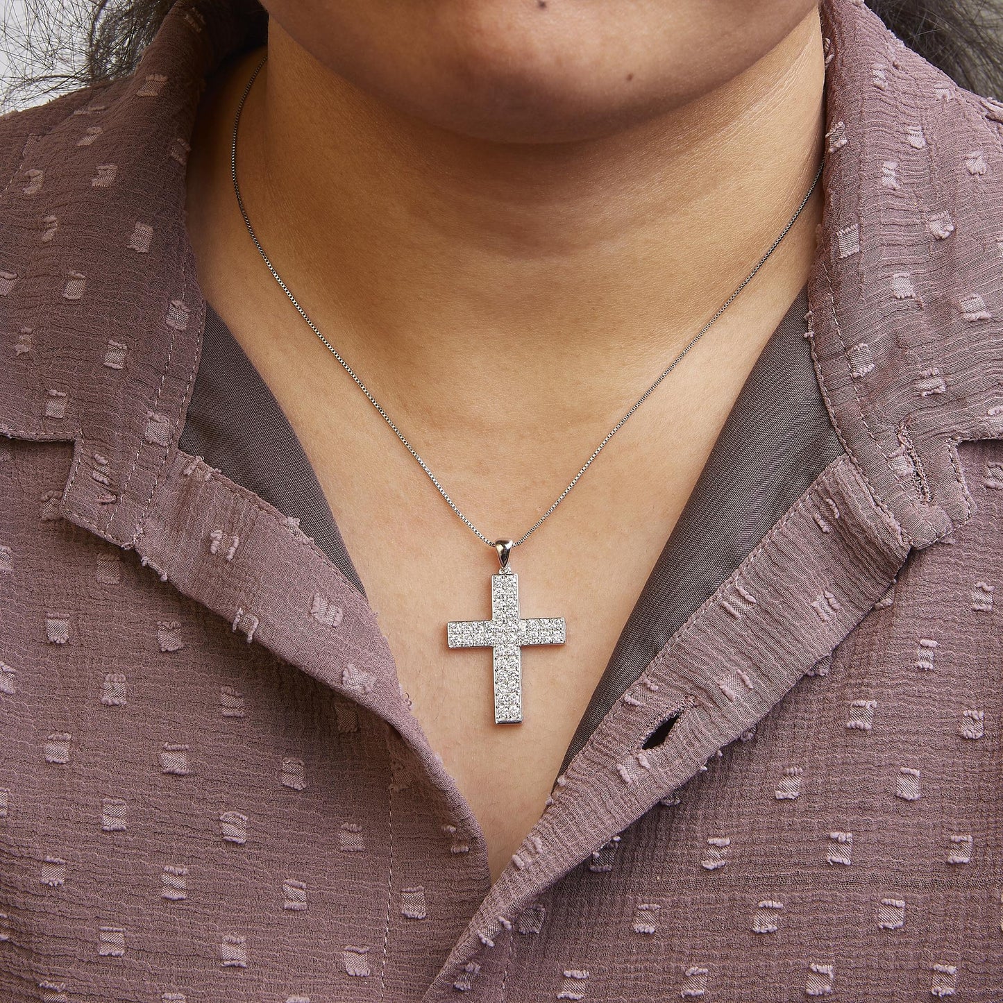 Front view of a white metal necklace with a cross-shaped pendant adorned with round white gemstones in prong setting, worn on a model.