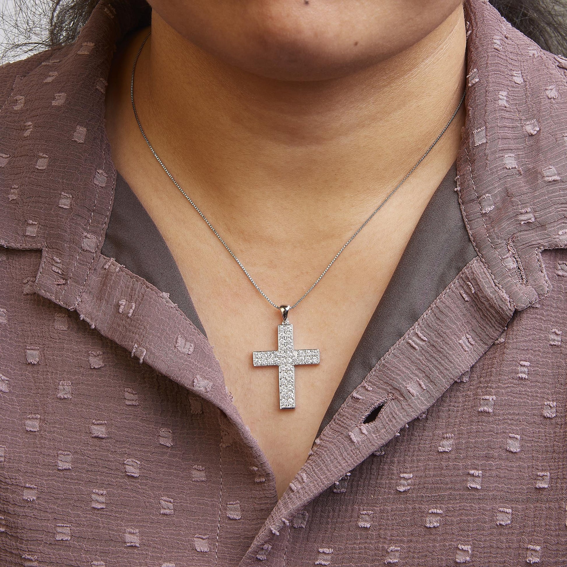 Front view of a white metal necklace with a cross-shaped pendant adorned with round white gemstones in prong setting, worn on a model.
