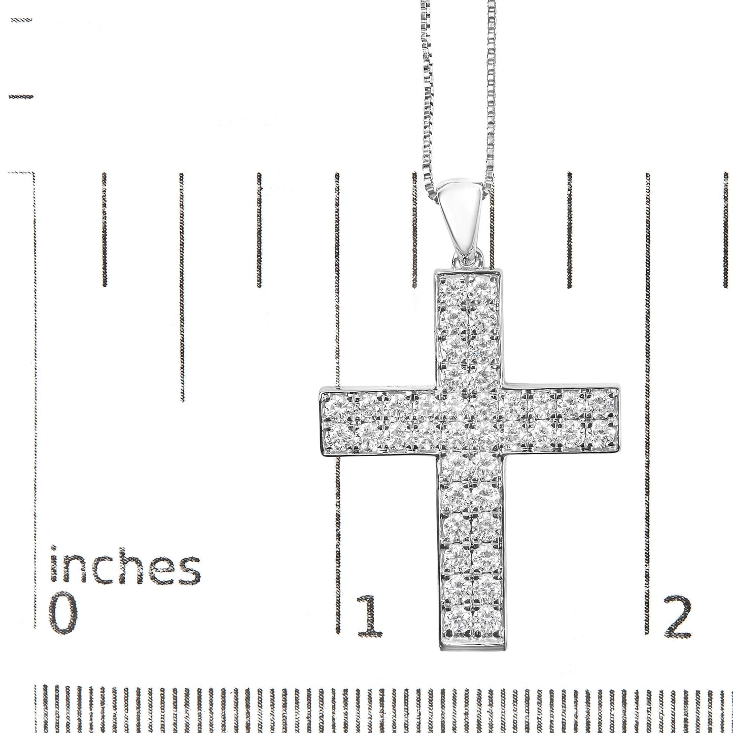 Close-up front view of a white metal cross-shaped necklace pendant set with round white gemstones in prong settings, displayed on a ruler for size reference.