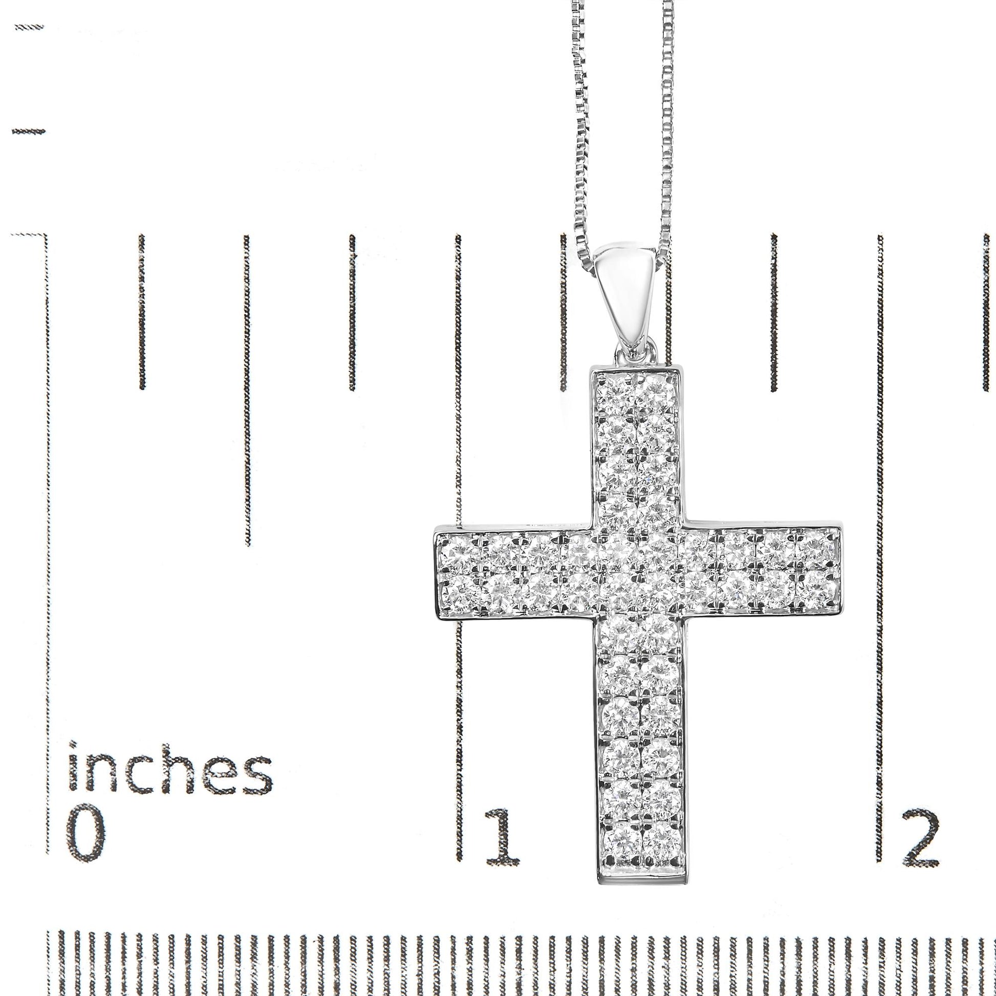 Close-up front view of a white metal cross-shaped necklace pendant set with round white gemstones in prong settings, displayed on a ruler for size reference.