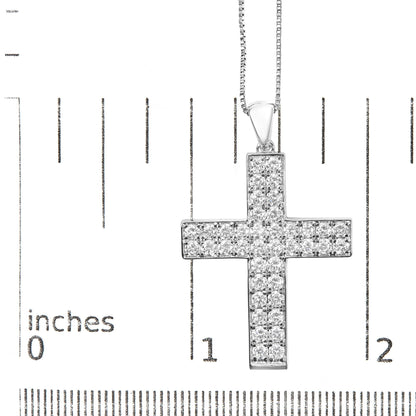 Close-up front view of a white metal cross-shaped necklace pendant set with round white gemstones in prong settings, displayed on a ruler for size reference.