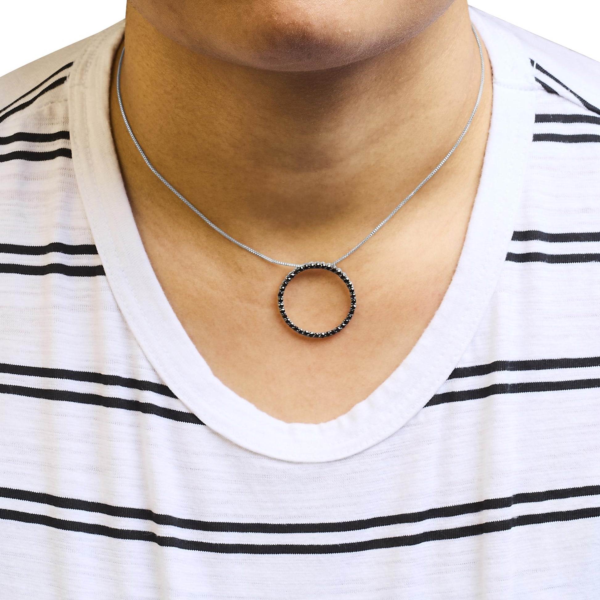 Close-up front view of a white metal necklace with a circular pendant featuring black round gemstones in shared prong setting, worn on a model.