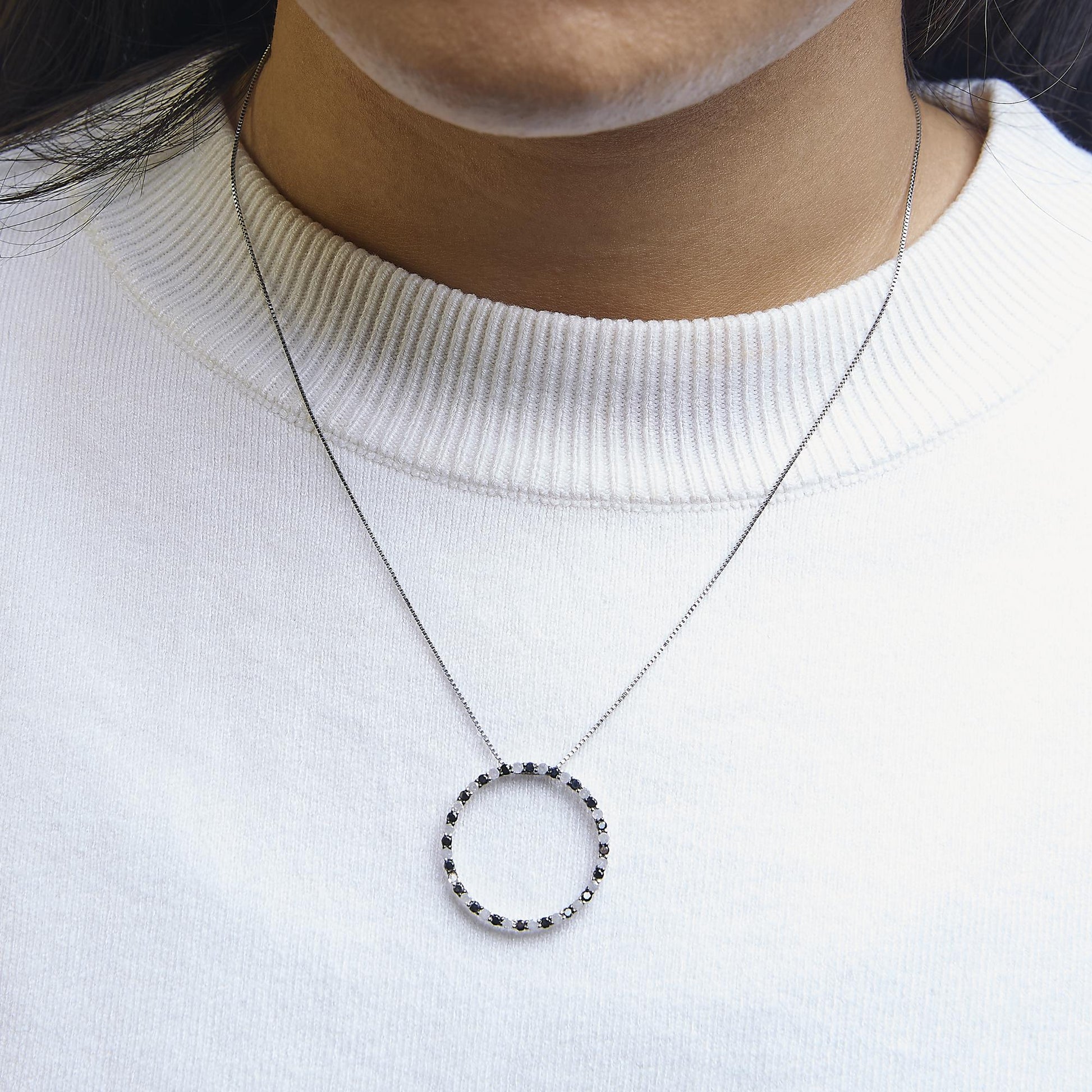 Close-up front view of a white metal necklace with a circular pendant set with alternating black and white round gemstones, shown worn on a model.