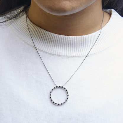 Close-up front view of a white metal necklace with a circular pendant set with alternating black and white round gemstones, shown worn on a model.